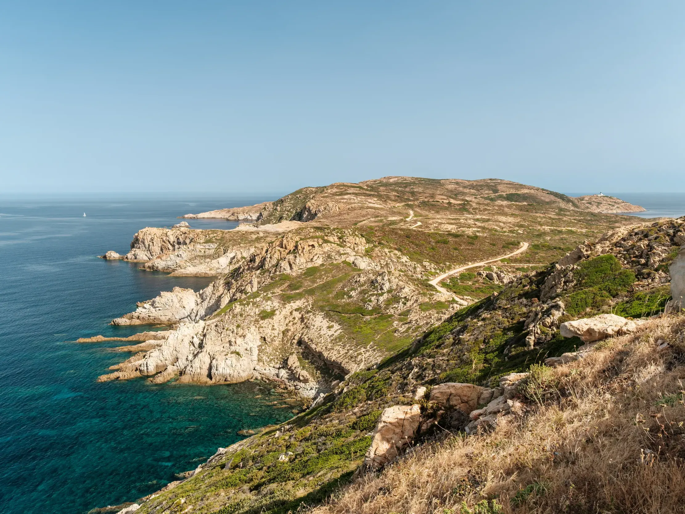 Panoramablick beim Wandern auf die Halbinsel La Revellata bei Calvi mit Felsküste, türkisem Meer und Leuchtturm am Horizont.