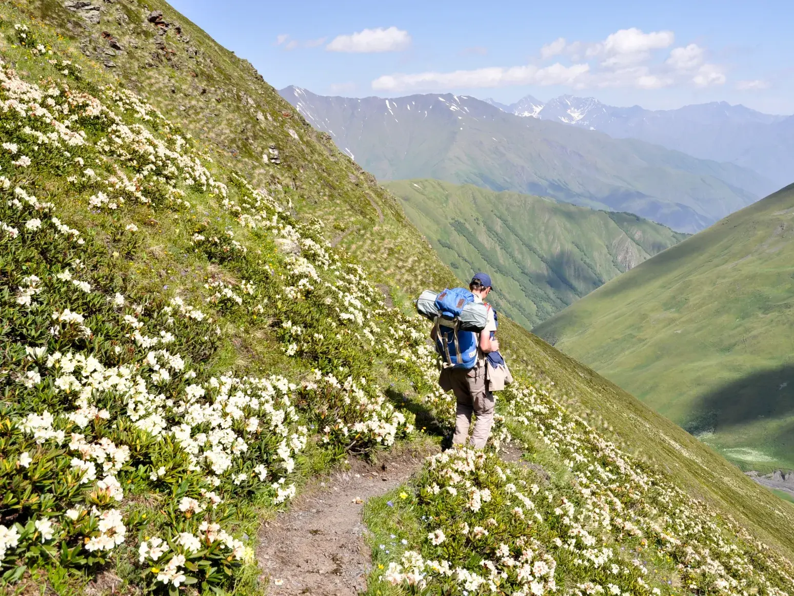 Wanderer mit großem Rucksack auf einem schmalen Pfad am Rhododendron-Berg mit Blick auf die Berge des Kaukasus in Georgien.