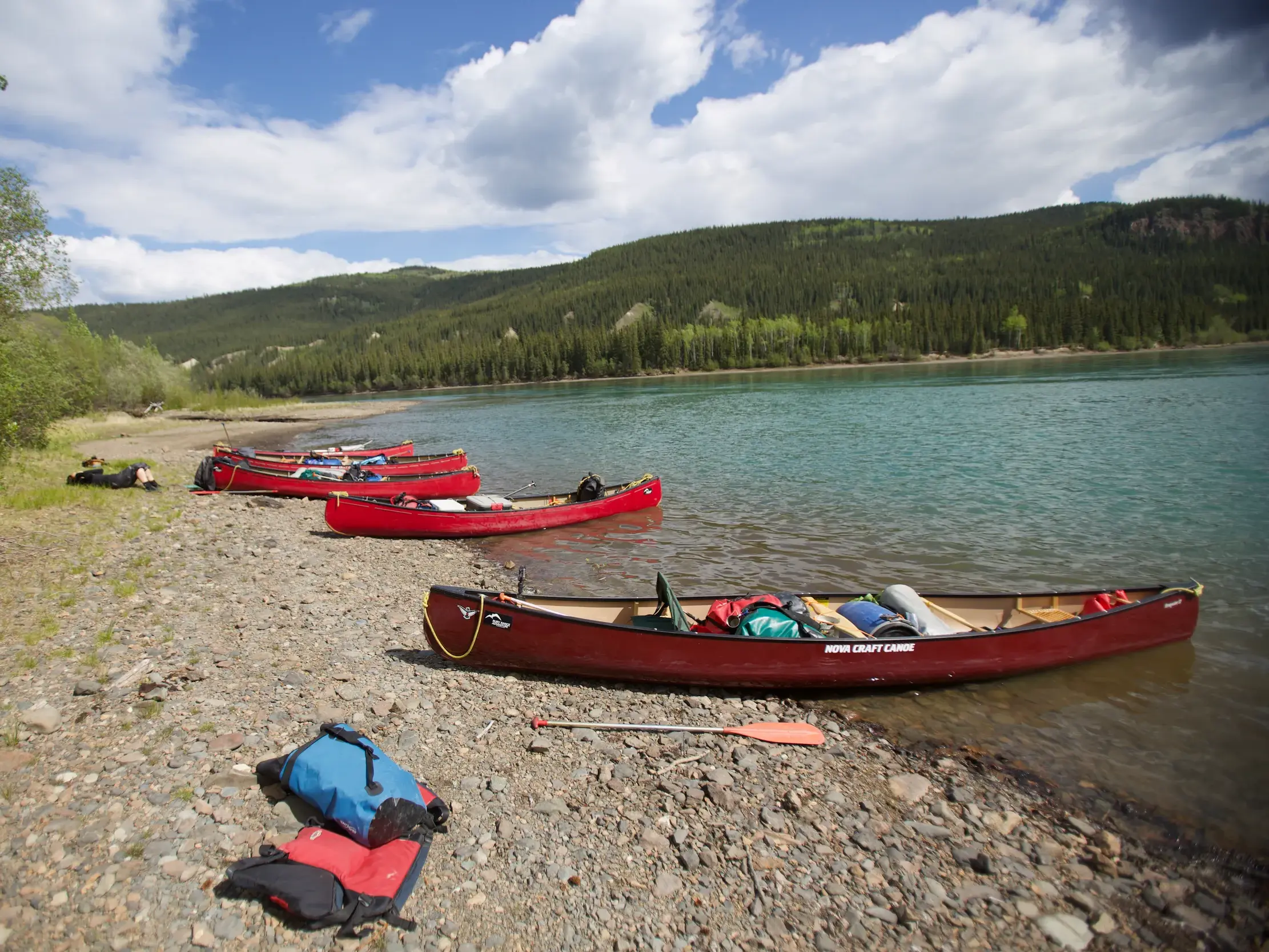 Rote Kanus bei einer Pause am Kiesufer des türkisfarbenen Yukon River während eines Kanutrekkings in Kanada.