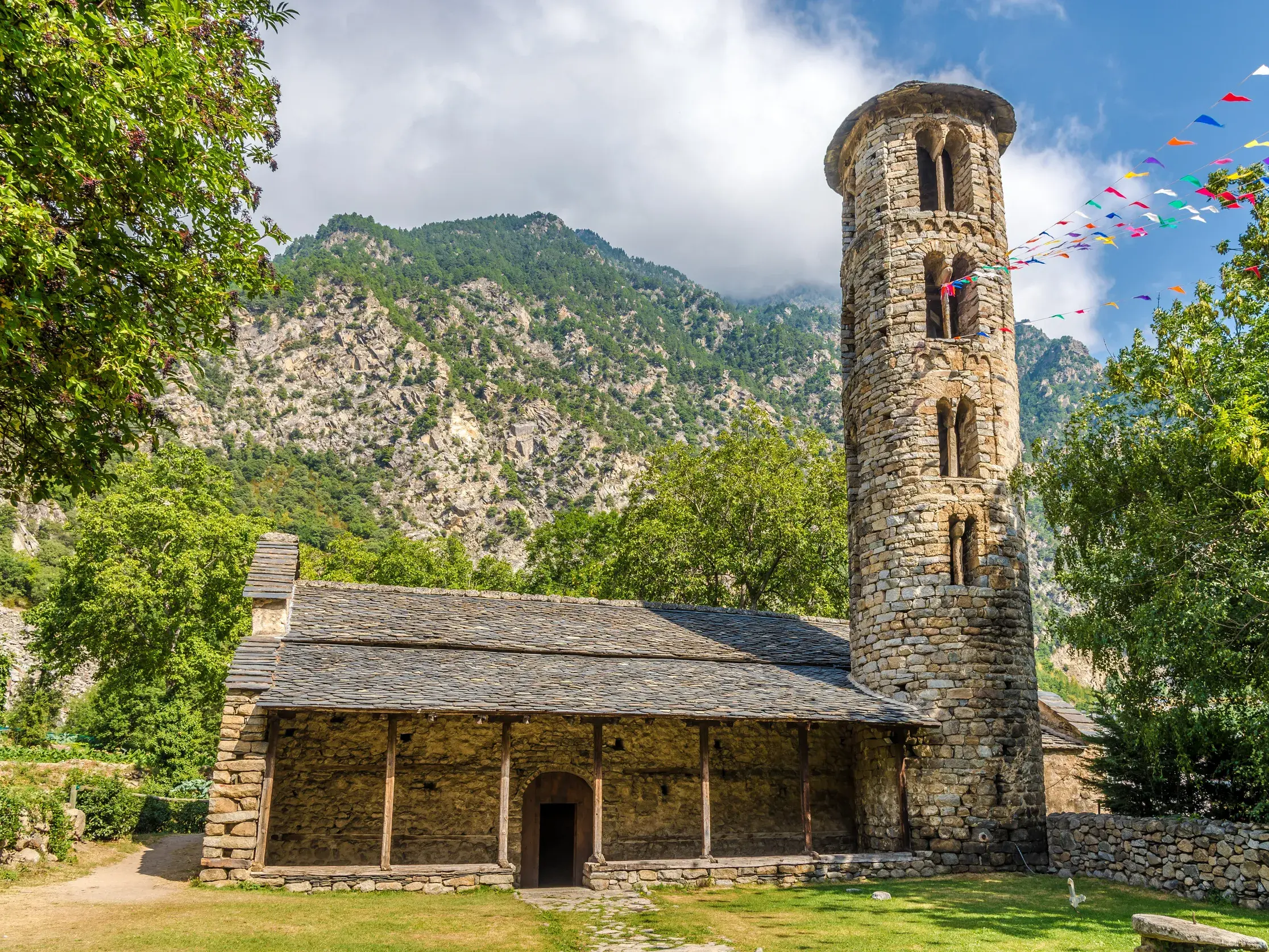 Die historische, romanische Kirche Santa Coloma in Andorra mit ihrem markanten, runden Glockenturm vor der Bergkulisse der Pyrenäen.
