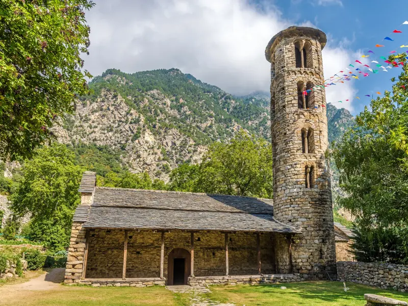 Die historische, romanische Kirche Santa Coloma in Andorra mit ihrem markanten, runden Glockenturm vor der Bergkulisse der Pyrenäen.