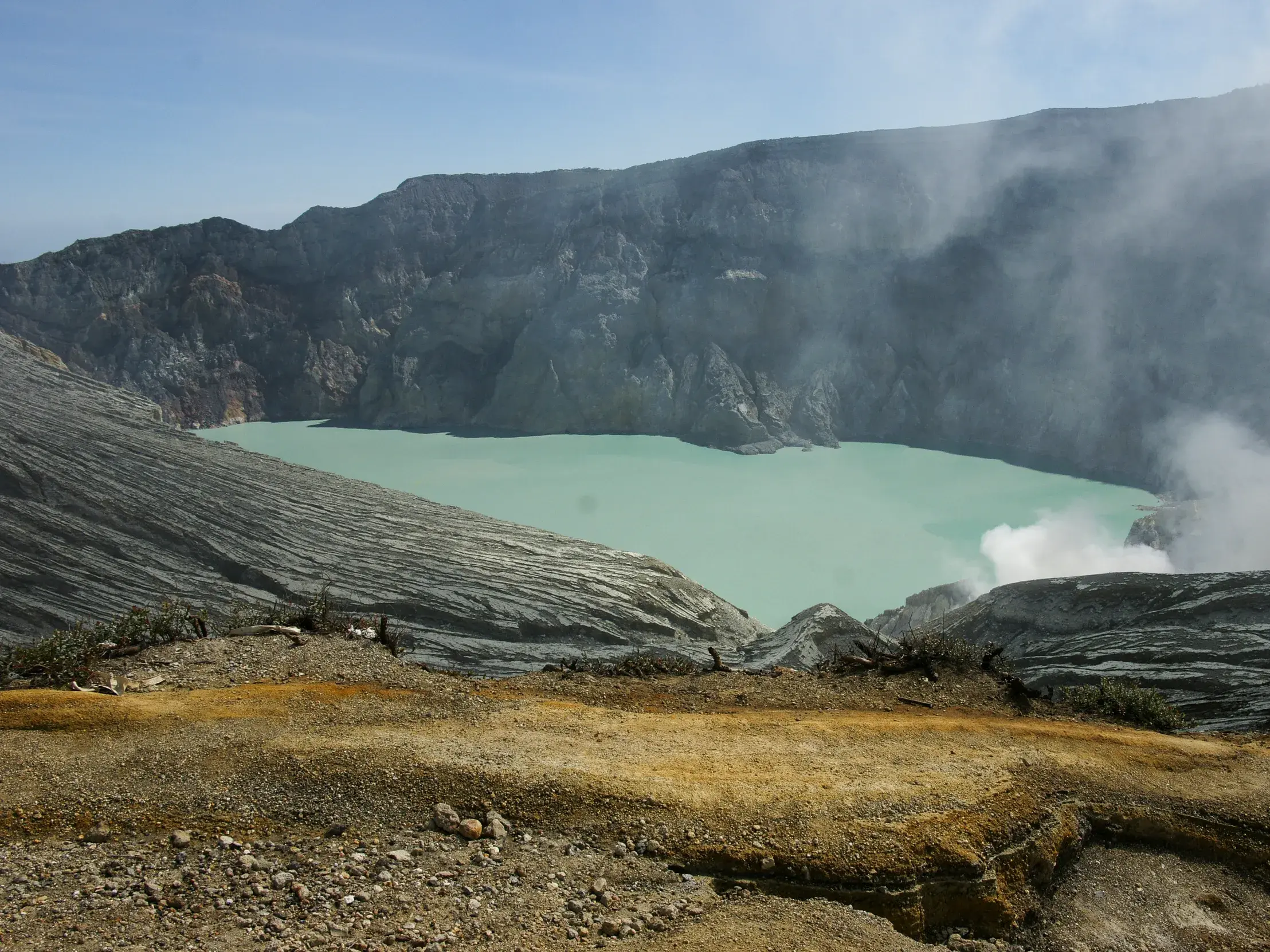 Blick vom Kraterrand auf den türkisblauen, dampfenden Ijen-Kratersee in der Vulkanlandschaft auf Java.
