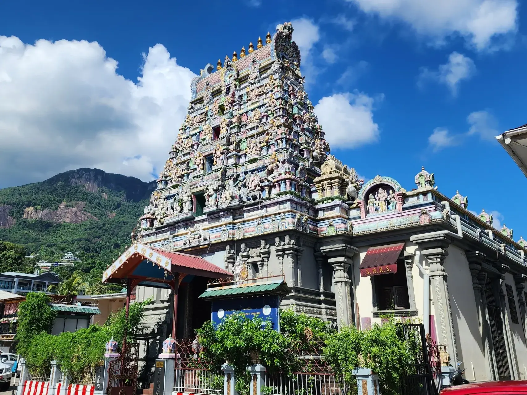 Farbenprächtiger, figurenreicher Hindu-Tempel in Victoria auf Mahé vor einem grünen Bergmassiv unter blauem Himmel.