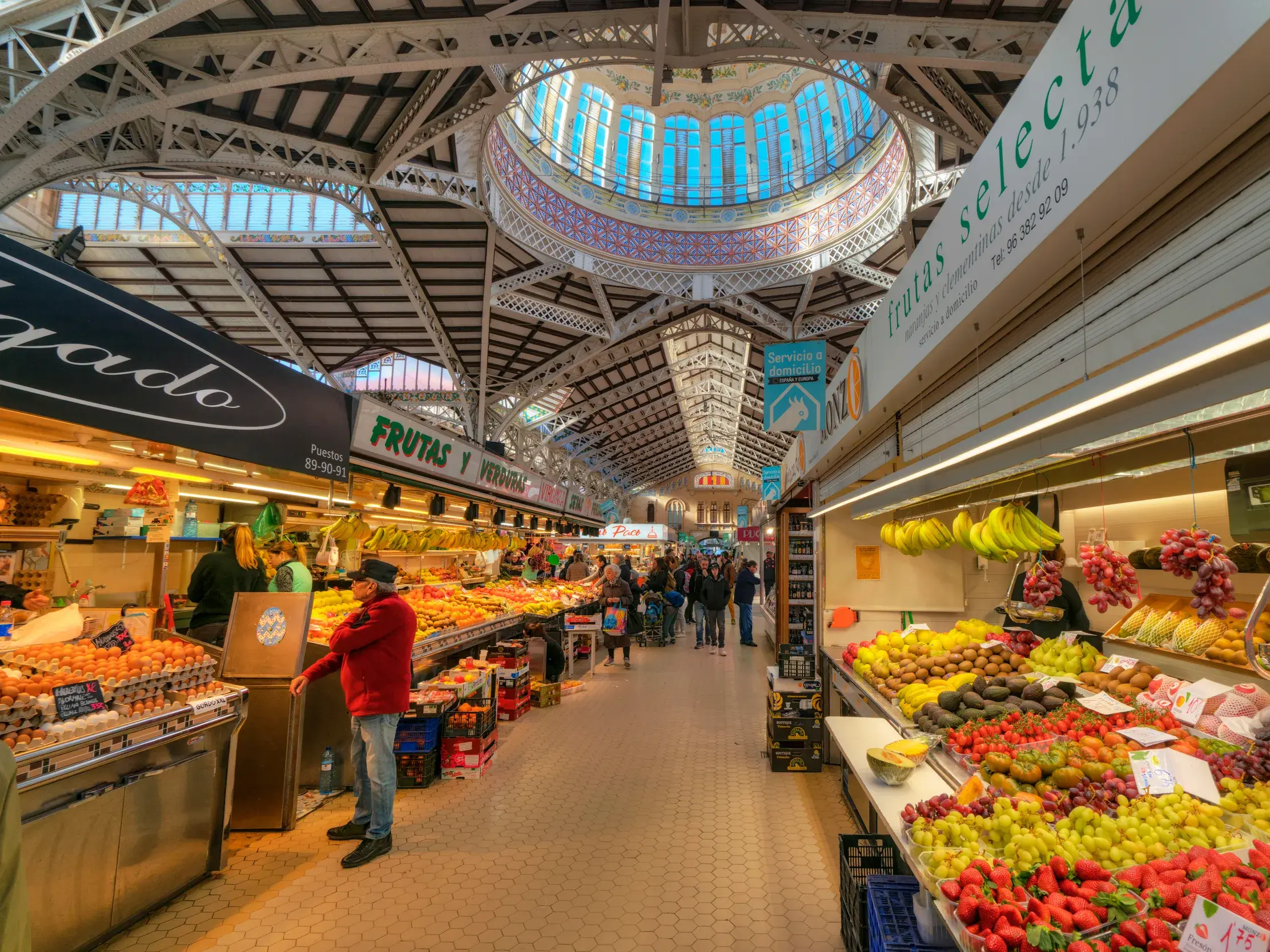 Lebhaftes Treiben im Mercado Central in Valencia: Besucher schlendern entlang der Stände mit frischem Obst unter der Kuppel.