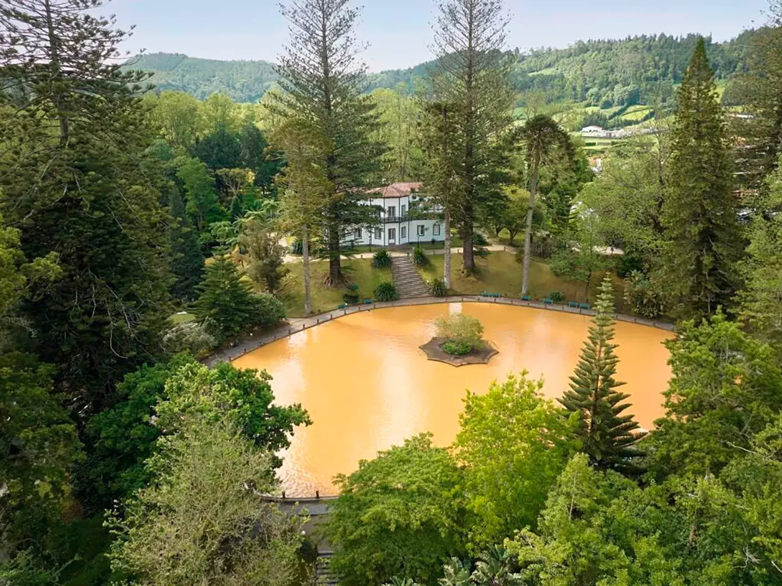 Der orangefarbene Thermal-See in der grünen Parkanlage von Furnas auf der Azoren-Insel Sao Miguel mit einem Landhaus.