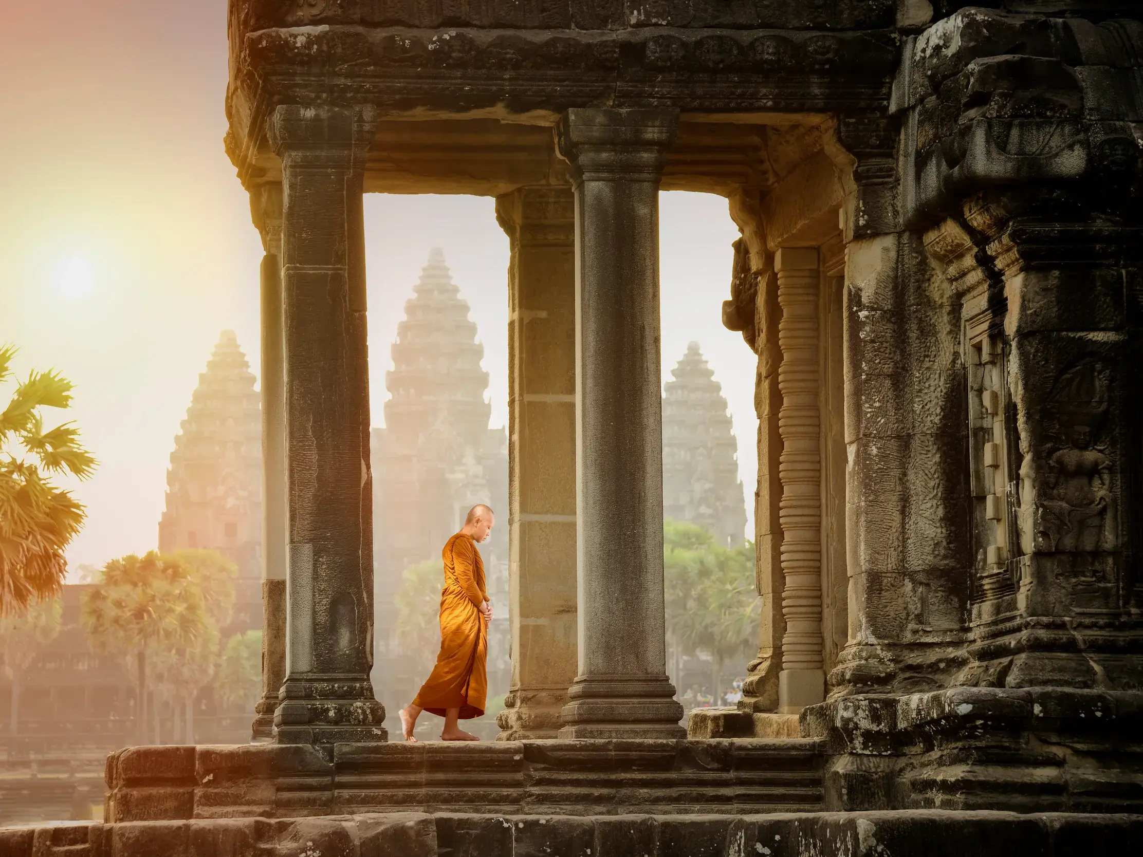 Ein barfüßiger Mönch in safranfarbener Robe geht durch eine Steingalerie in Angkor Wat, Kambodscha, im goldenen Morgenlicht.