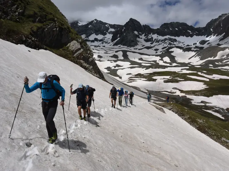Eine Hauser-Wandergruppe mit Bergführer durchquert ein Schneefeld bei einer Alpenüberquerung in den Hohen Tauern.