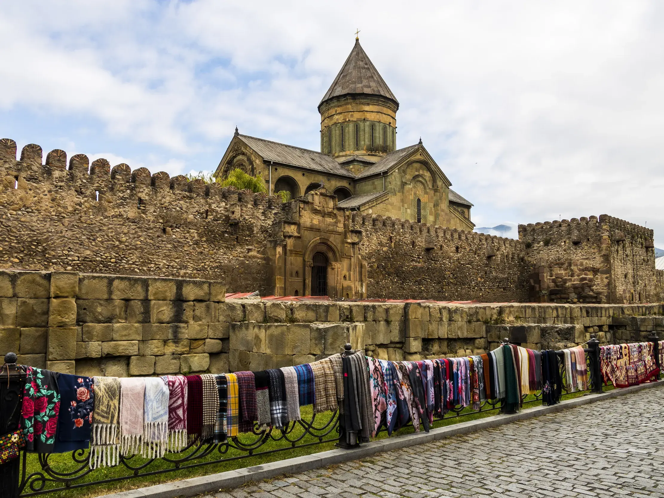 Steinerne Wehrmauer der Swetizchoweli-Kathedrale in Mzcheta. Davor werden bunte Schals auf der Wanderreise verkauft.