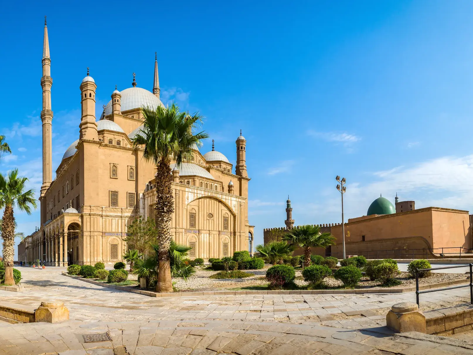 Weitwinkelaufnahme der Alabaster-Moschee in der Saladins Zitadelle in Kairo, umgeben von Palmen und einem gepflasterten Vorplatz.