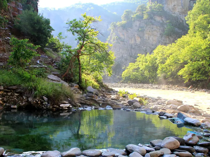 Natürlicher, steingefasster Pool der Thermalquellen von Benjë neben einem Fluss in einer sonnigen Schlucht in Albanien.