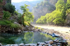 Natürlicher, steingefasster Pool der Thermalquellen von Benjë neben einem Fluss in einer sonnigen Schlucht in Albanien.