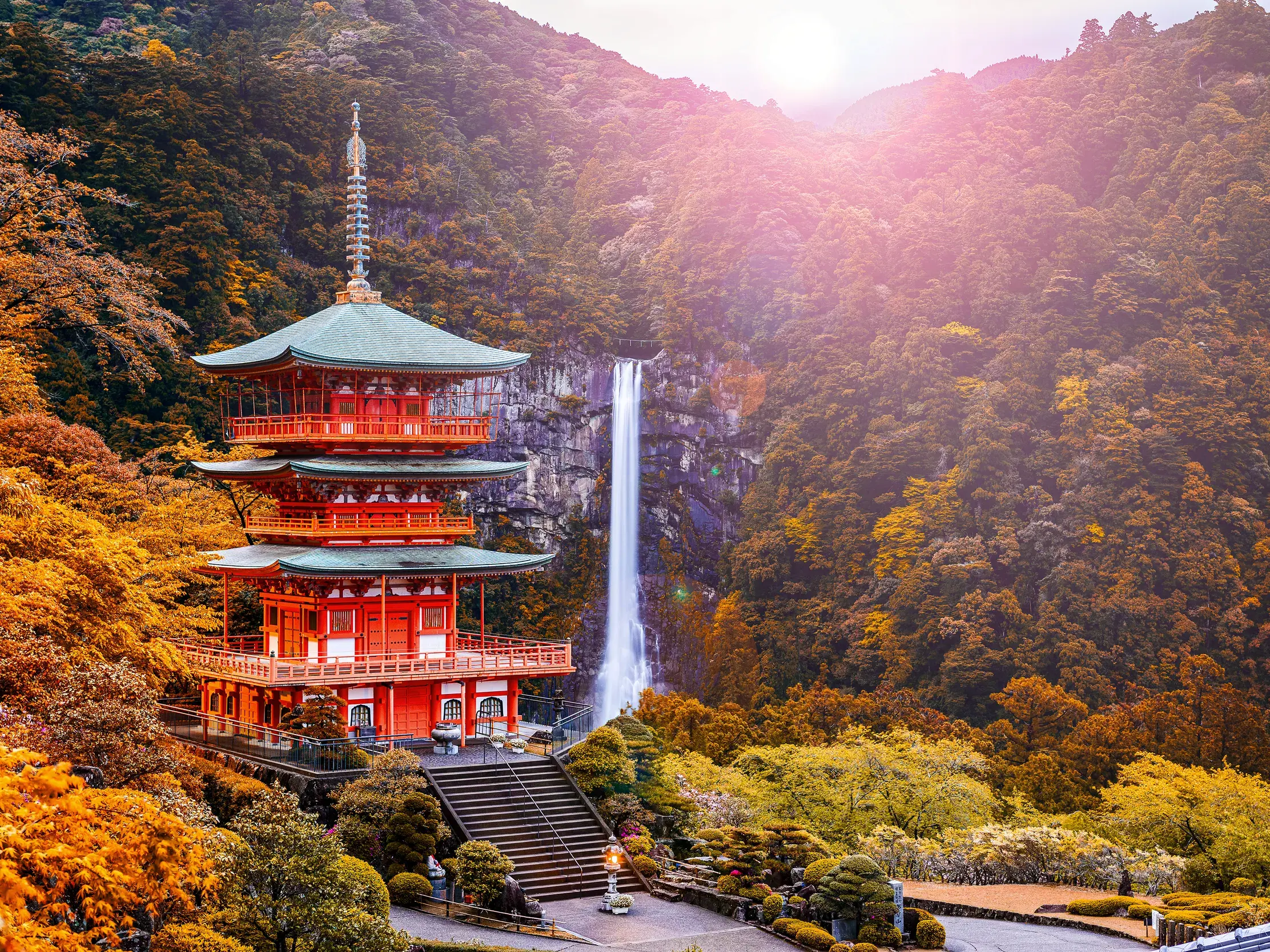 Die rote Pagode des Seiganto-ji Tempels vor dem Nachi-Wasserfall, umgeben von buntem Herbstlaub am Kumano Kodo Pilgerweg.