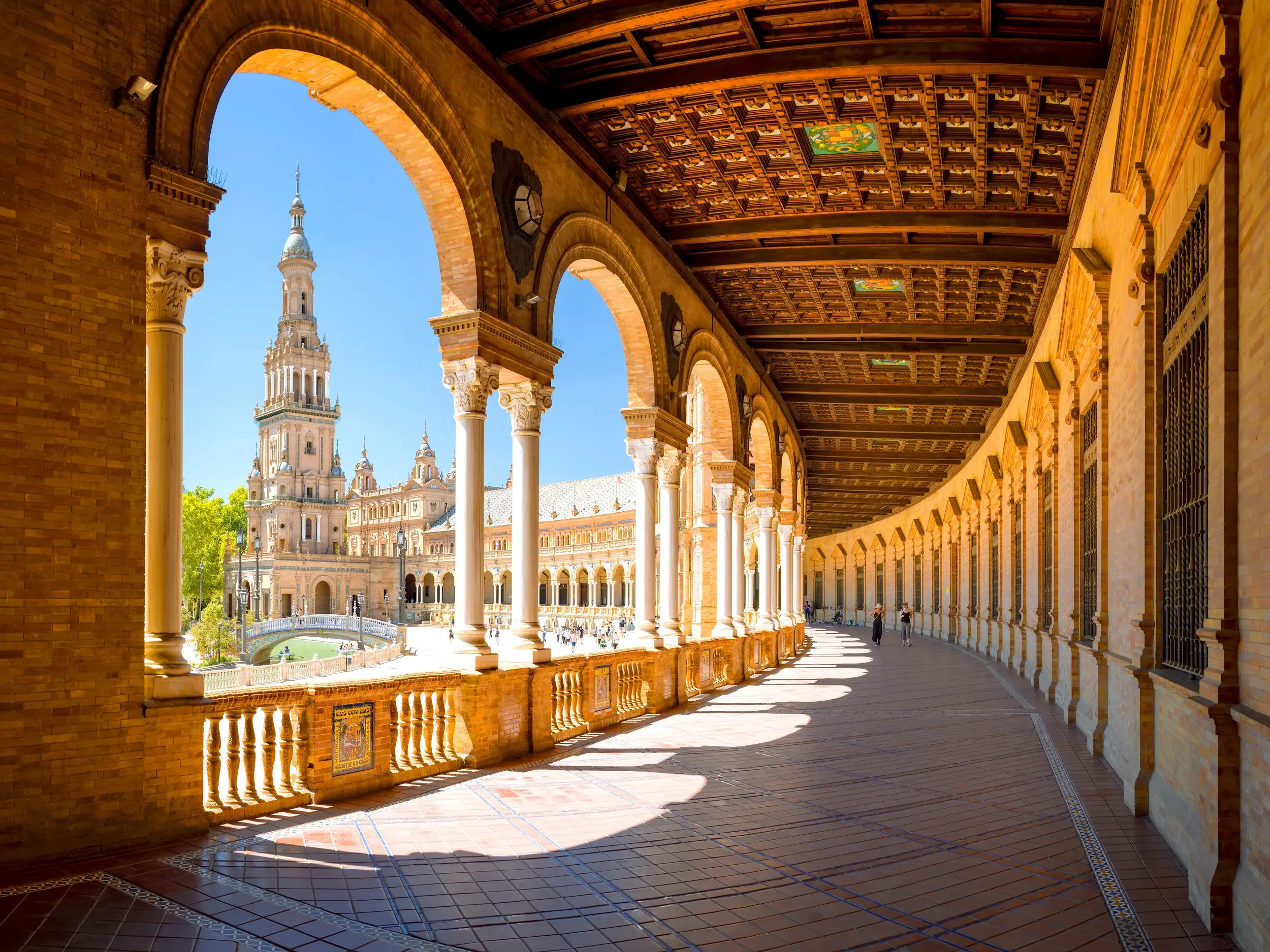 Beeindruckende Arkaden der Plaza de España in Sevilla mit detailreicher Kassettendecke und Blick auf den sonnigen Platz.