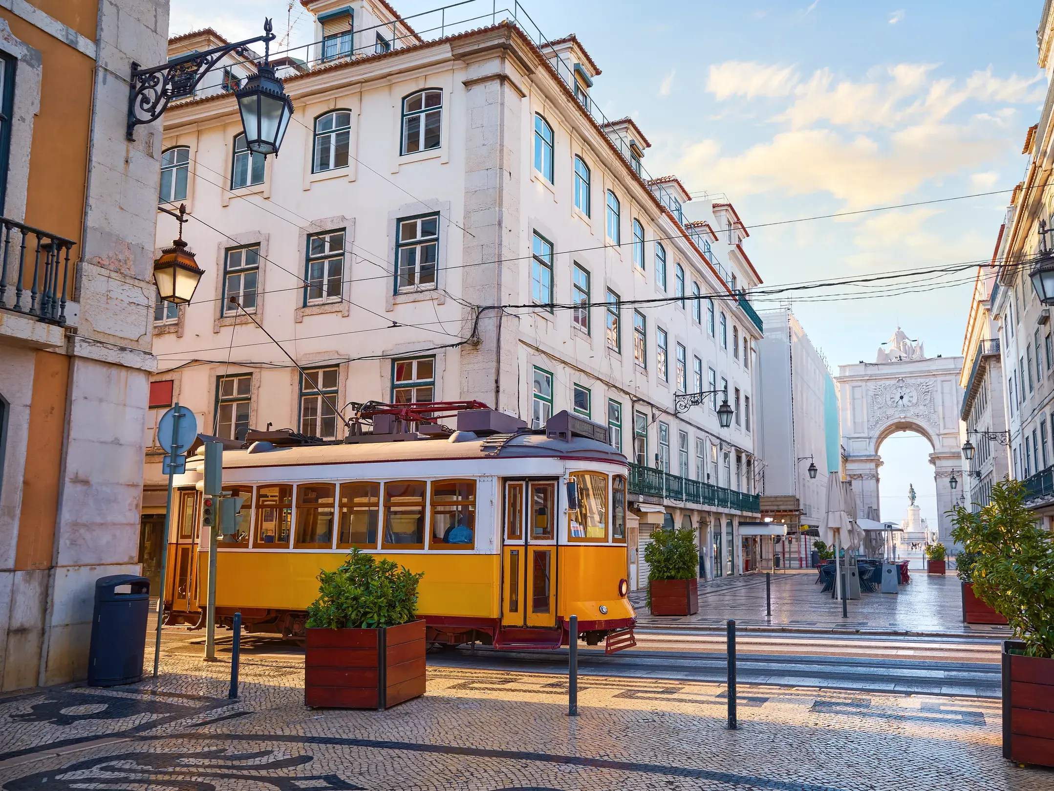 Historische gelbe Straßenbahn auf Kopfsteinpflaster in der Baixa von Lissabon mit dem Triumphbogen Arco da Rua Augusta.