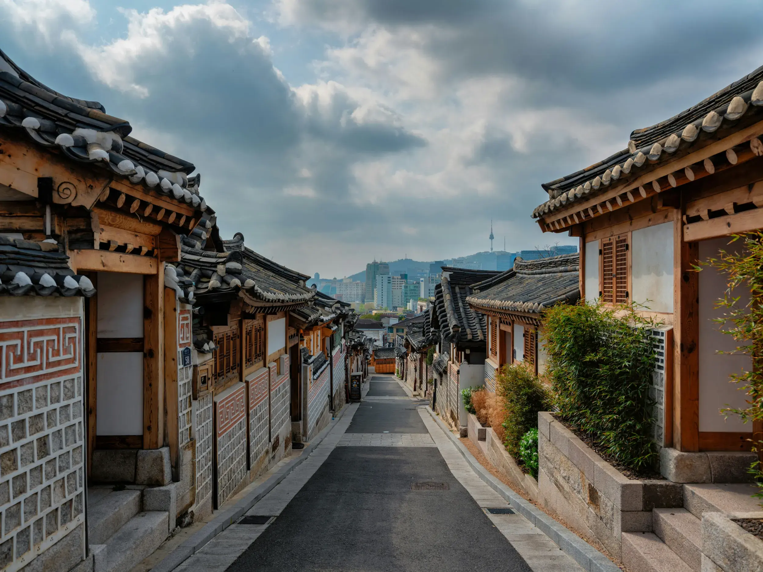 Traditionelle Hanok-Häuser in einer Gasse des Bukchon Village in Seoul mit Blick auf die moderne Skyline und den N Seoul Tower.