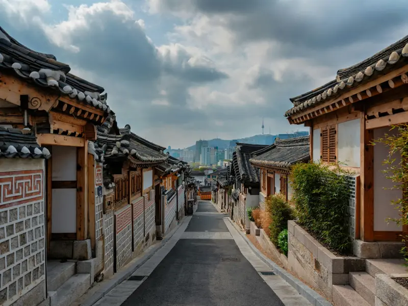 Traditionelle Hanok-Häuser in einer Gasse des Bukchon Village in Seoul mit Blick auf die moderne Skyline und den N Seoul Tower.