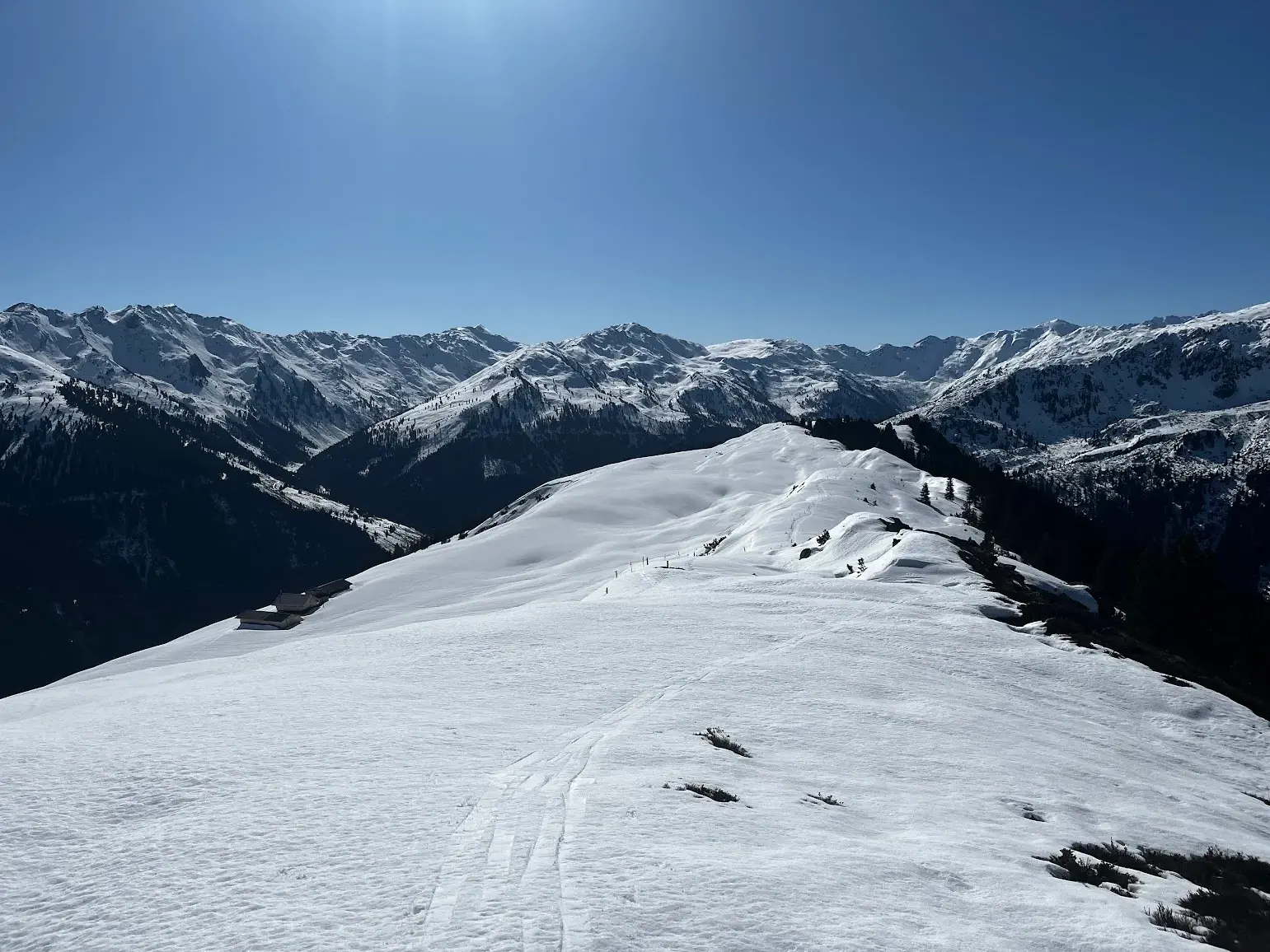 Spuren im Tiefschnee führen über einen Grat zum Panoramablick auf die winterlichen Gipfel der Kitzbüheler Alpen.