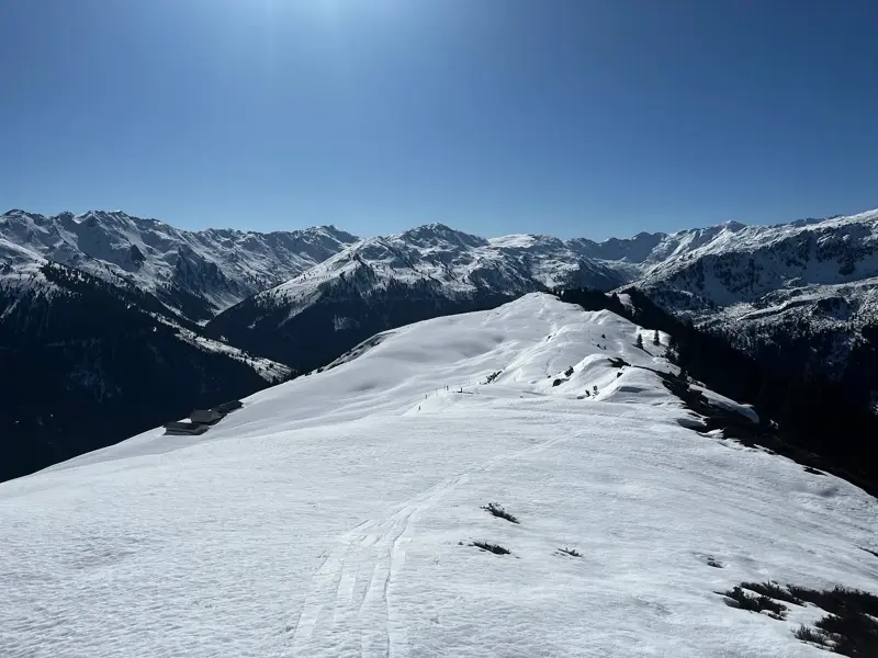 Ein schneebedeckter Berggrat in der Wildschönau mit Spuren einer Schneeschuhwanderung und Panoramablick auf die Kitzbüheler Alpen.