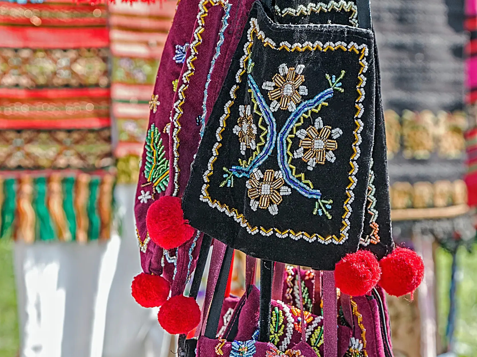 Farbenfrohe, traditionelle Handwerkskunst aus Rumänien: handbestickte Umhängetaschen mit Perlenmustern und roten Pompons.
