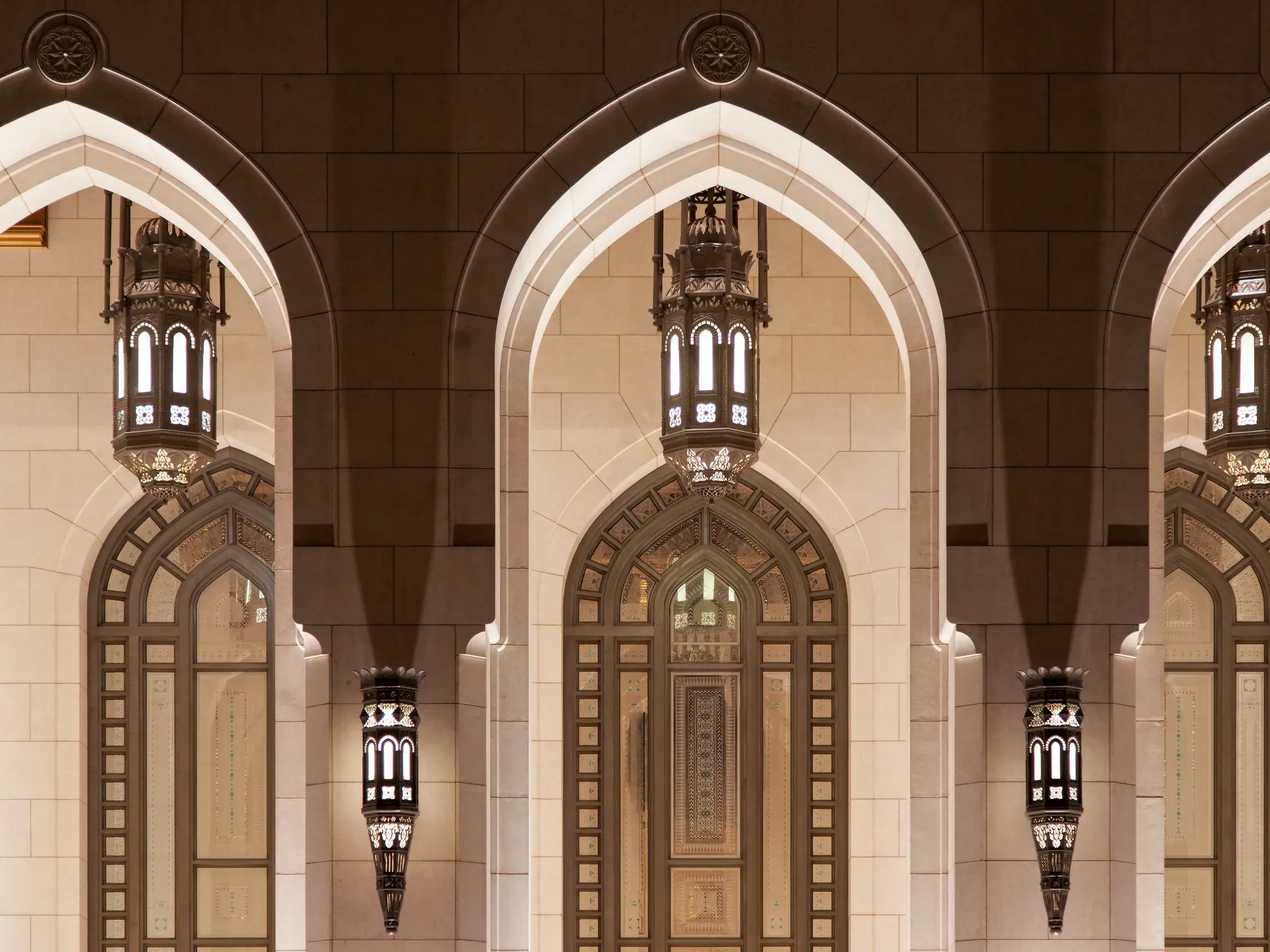 Prunkvolle, beleuchtete Arkaden mit kunstvollen Laternen in der Sultan-Qaboos-Moschee in Maskat bei Nacht.