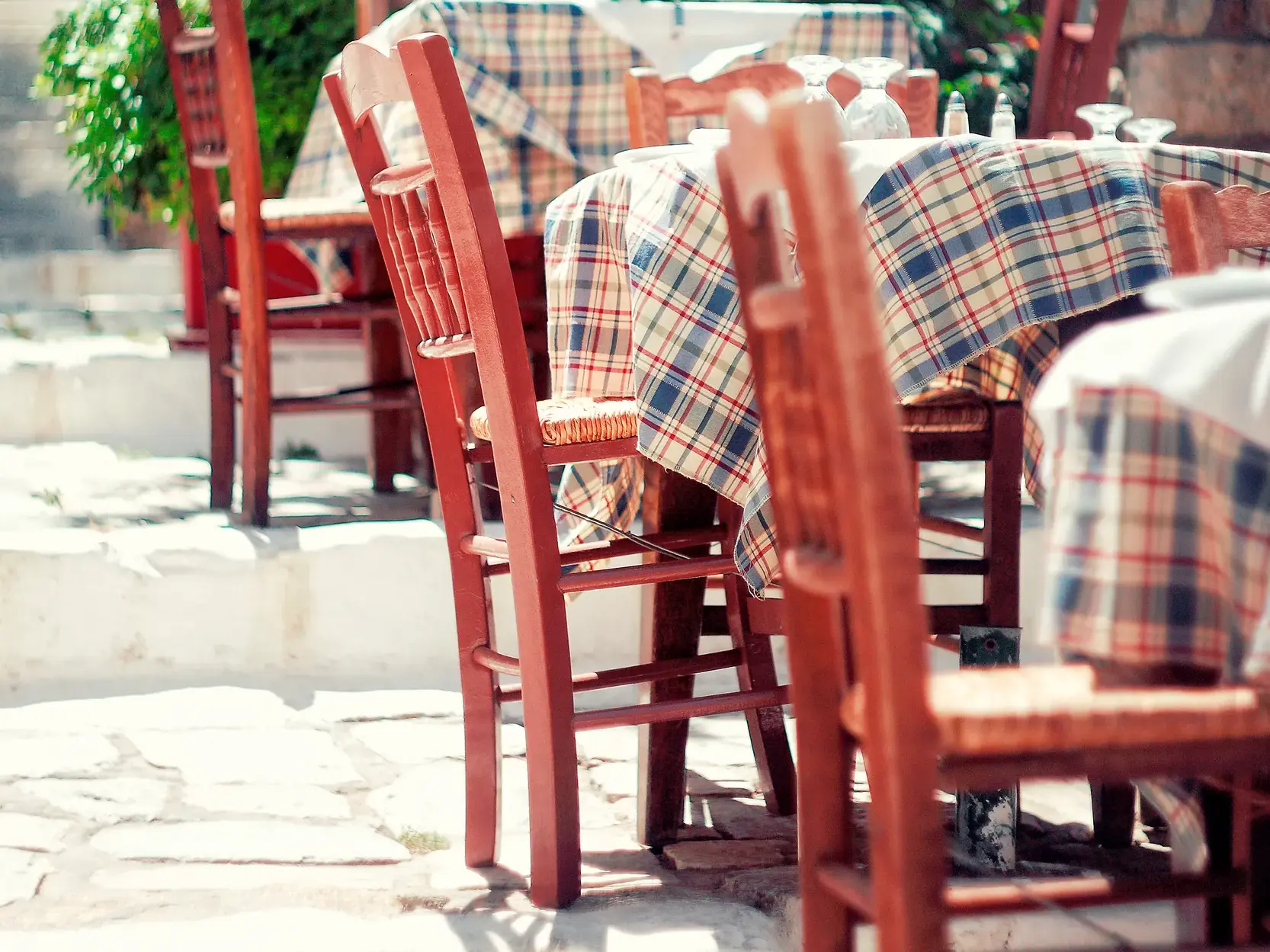 Gedeckte Tische mit karierten Decken und rote Holzstühle in einer sonnigen, urigen Taverne in der Altstadt Plaka in Athen.