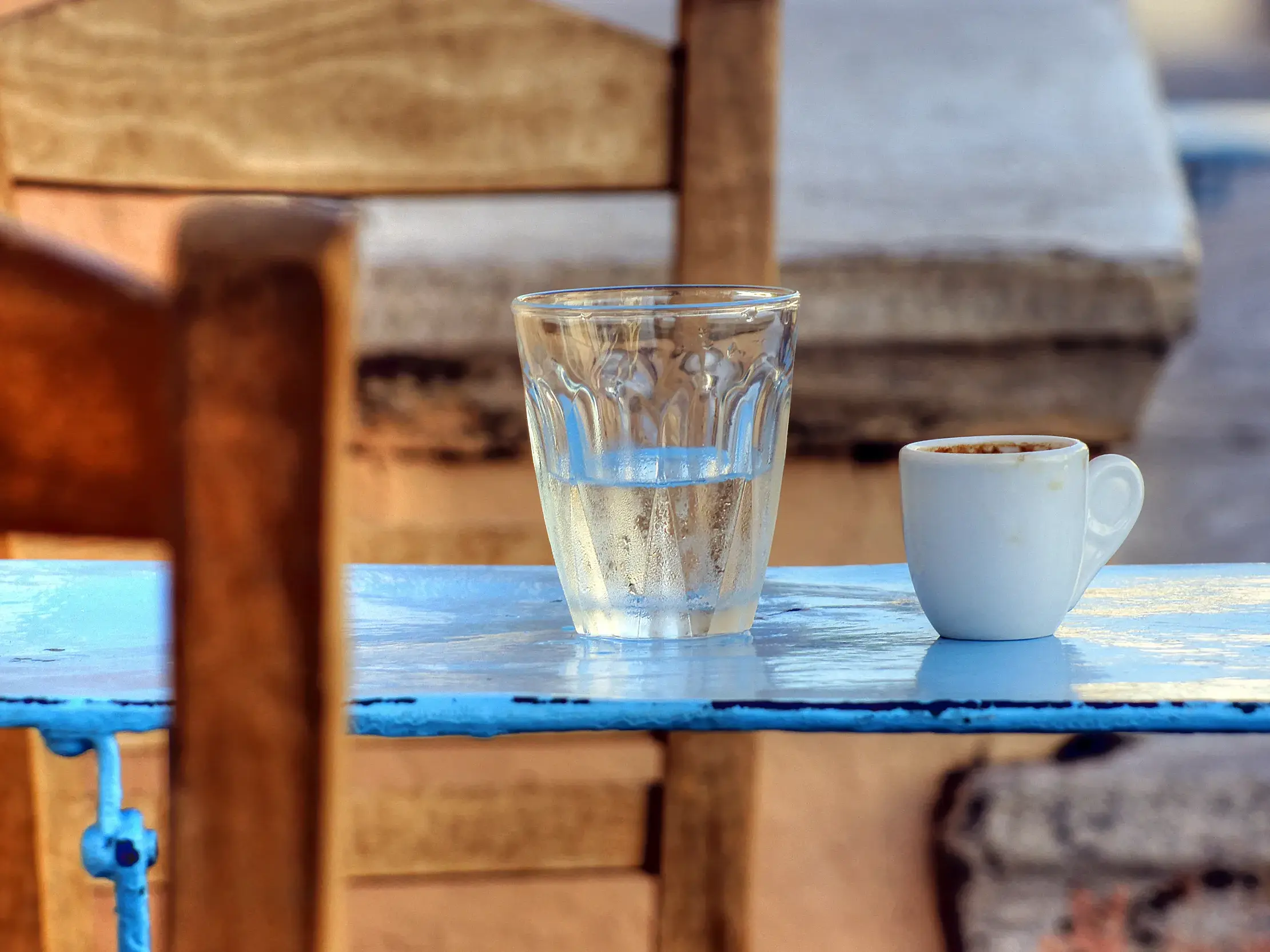 Griechischer Kaffee und ein Glas Wasser auf einem blauen Holztisch in einer landestypischen Taverne auf den Kykladen.