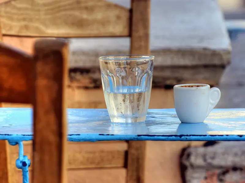 Griechischer Kaffee und ein Glas Wasser auf einem blauen Holztisch in einer landestypischen Taverne auf den Kykladen.