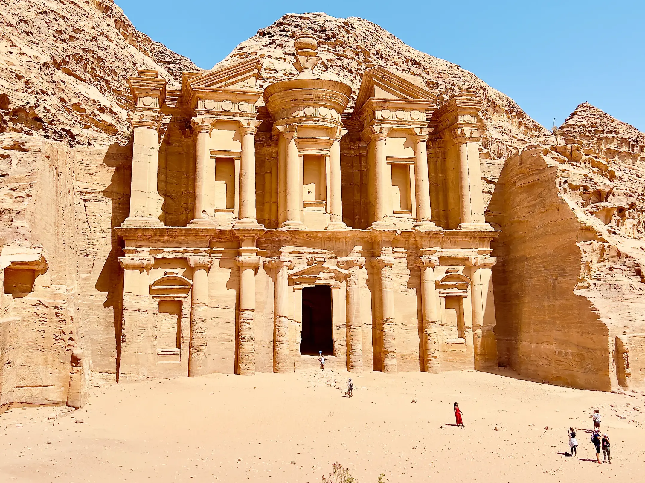 Imposante Fassade des in den Fels gehauenen Klosters Ad-Deir in Petra, Jordanien, mit Besuchern davor.