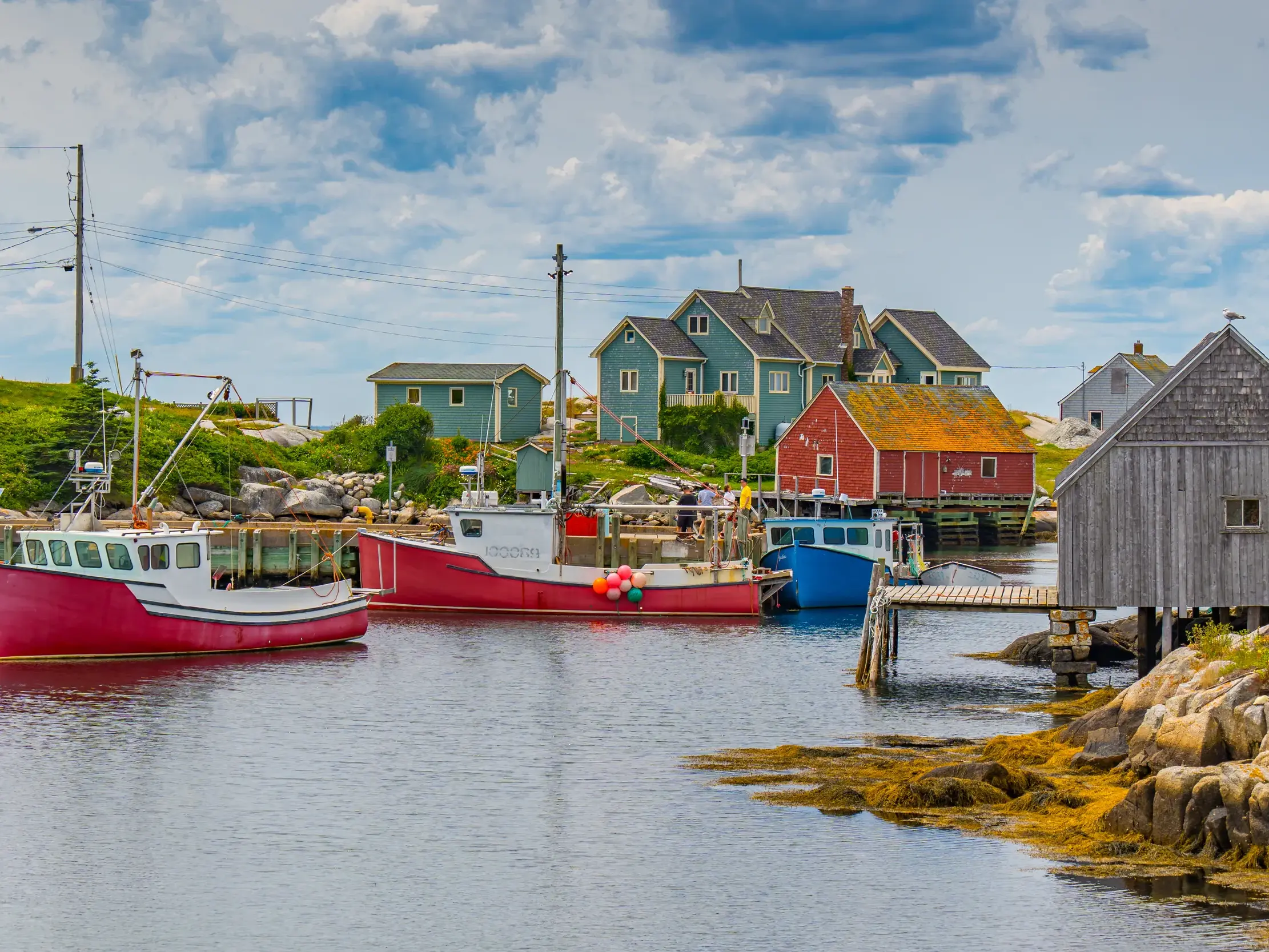 Rote Fischerboote liegen im Hafen des Dorfs Peggy's Cove vor bunten Holzhäusern an der felsigen Küste von Nova Scotia.