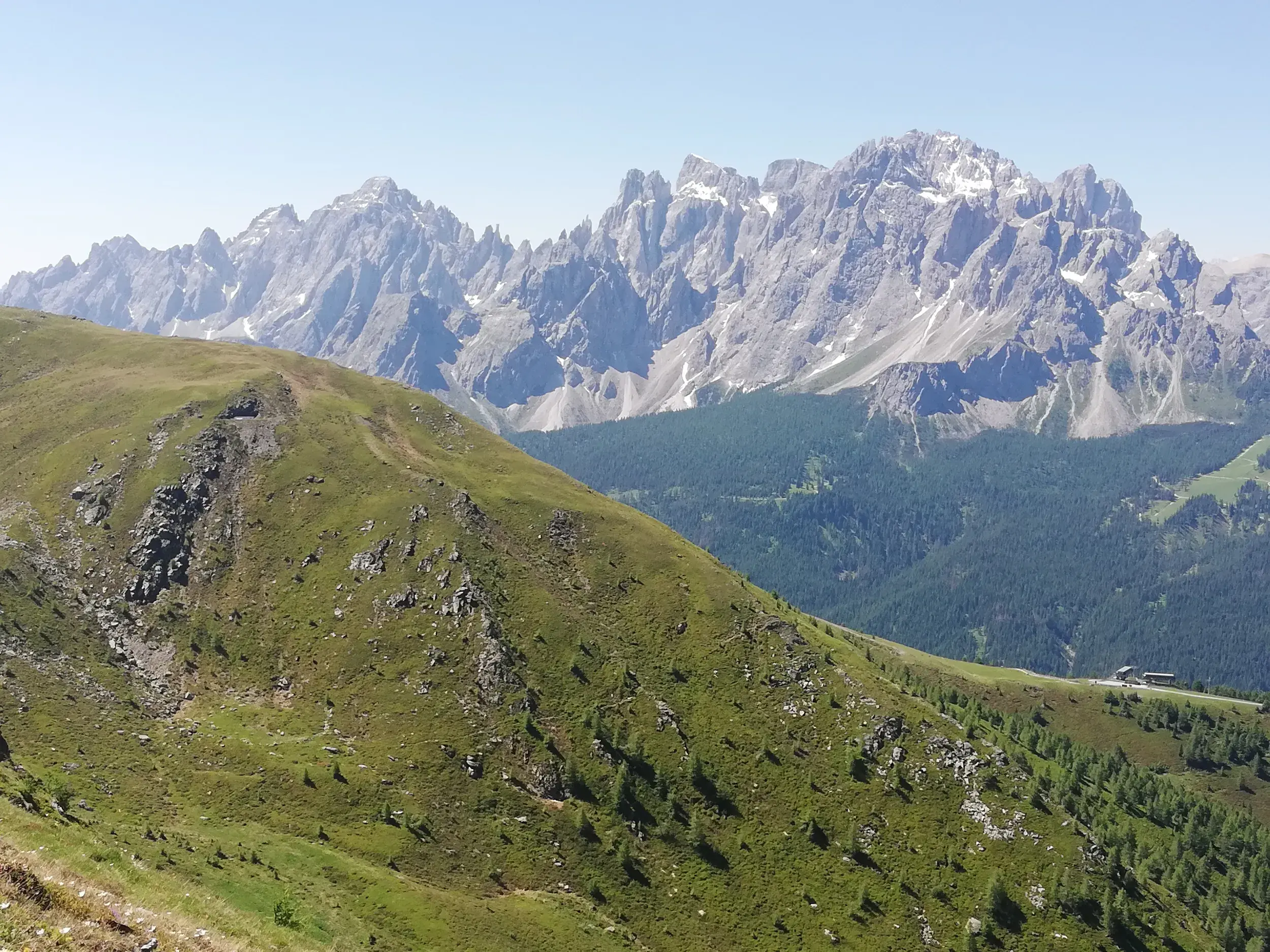Ein Wanderweg führt über einen grünen Bergkamm mit Blick auf die schroffen Felsgipfel der Südtiroler Dolomiten in den Karnischen Alpen.