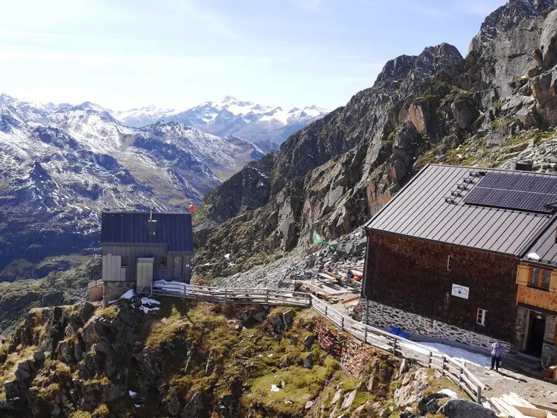 Die Hildesheimer Hütte auf einem Felsvorsprung mit Panoramablick auf die verschneiten Gipfel der Stubaier Alpen.