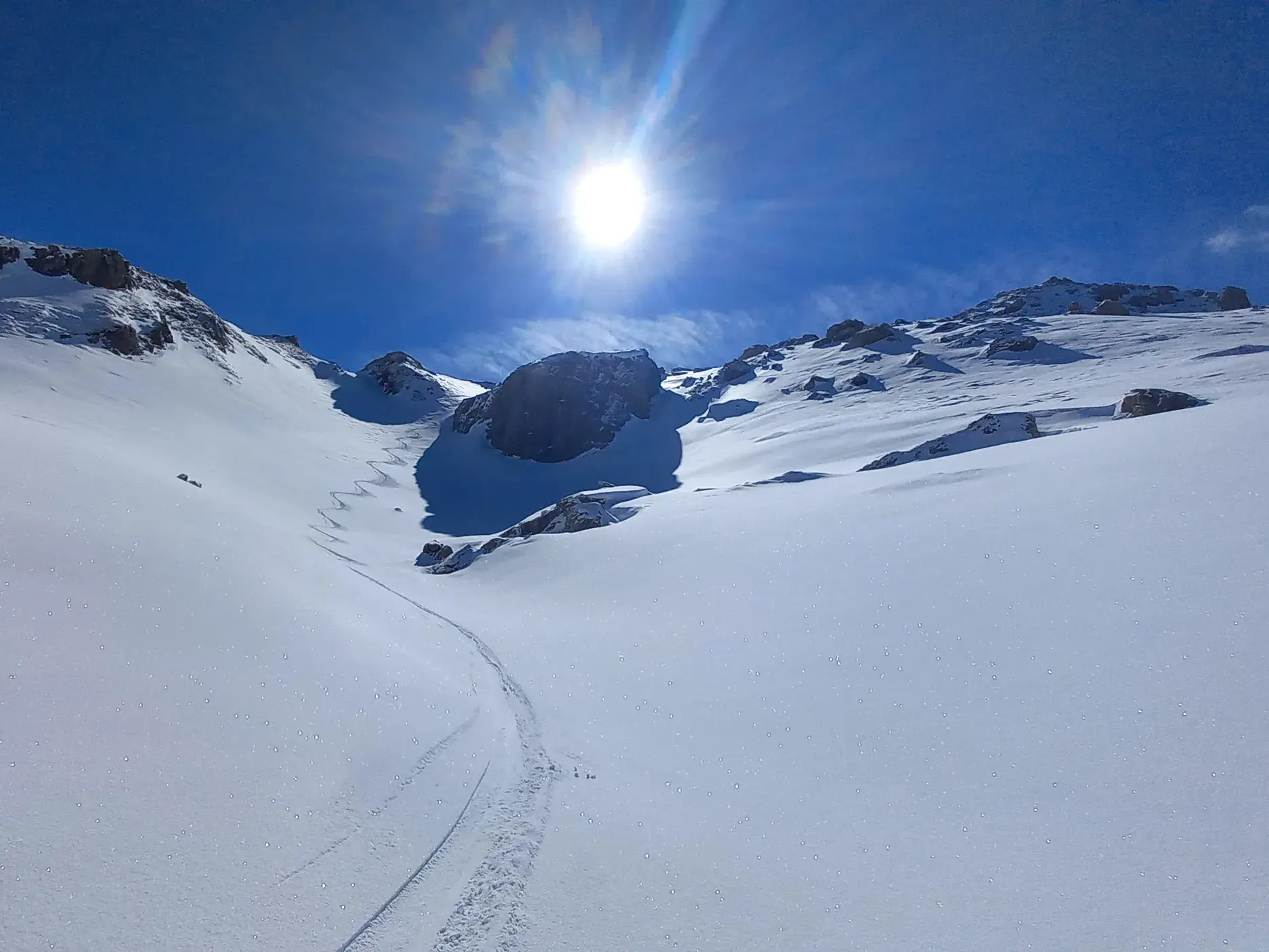 Eine Skispur zieht sich durch unberührten Pulverschnee einen weiten Hang im Sharr-Gebirge im Kosovo hinauf zur Sonne.