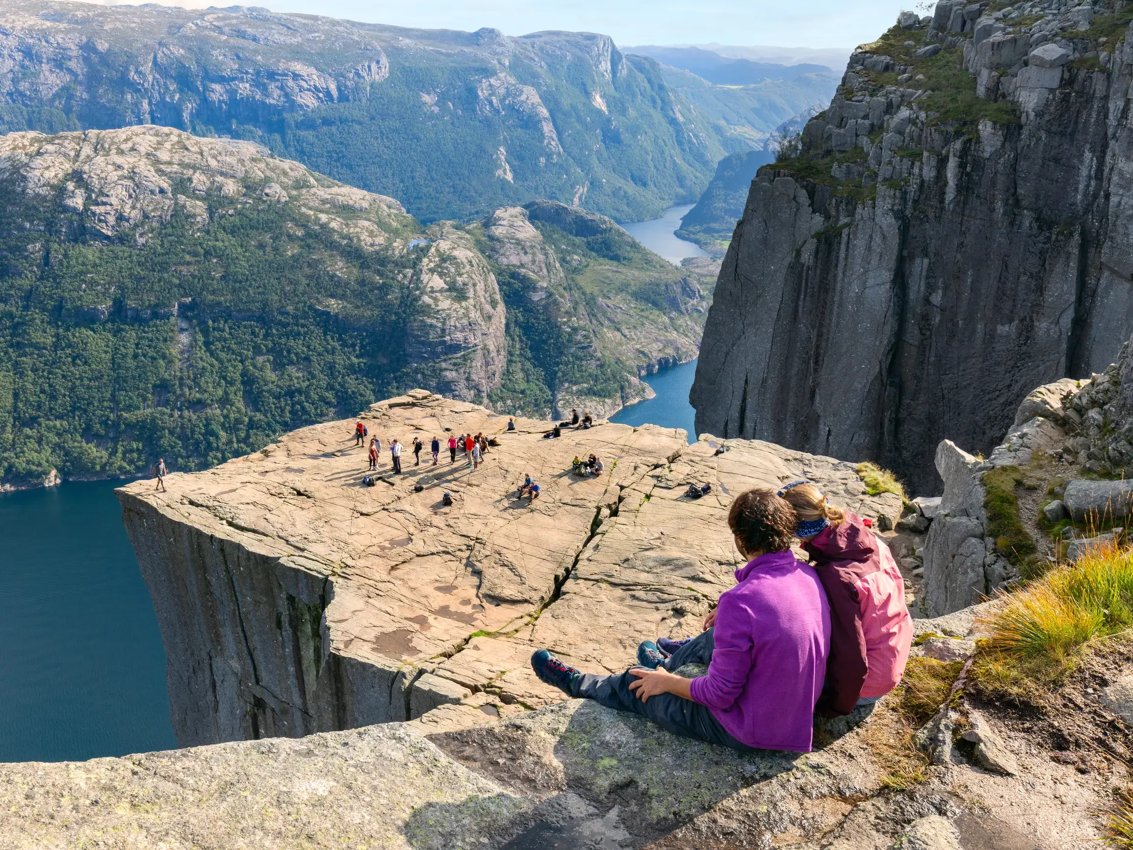 Junge Reisegruppe auf dem Felsplateau Preikestolen mit weitem Panoramablick über den blauen Lysefjord in Norwegen.