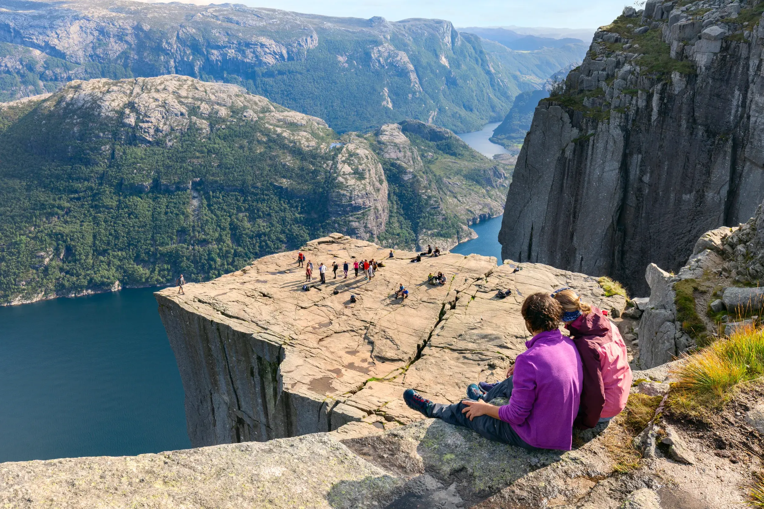 Junge Reisegruppe auf dem Felsplateau Preikestolen mit weitem Panoramablick über den blauen Lysefjord in Norwegen.