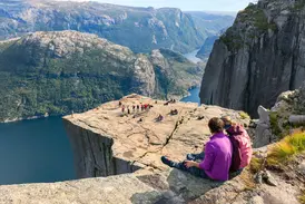 Junge Reisegruppe auf dem Felsplateau Preikestolen mit weitem Panoramablick über den blauen Lysefjord in Norwegen.
