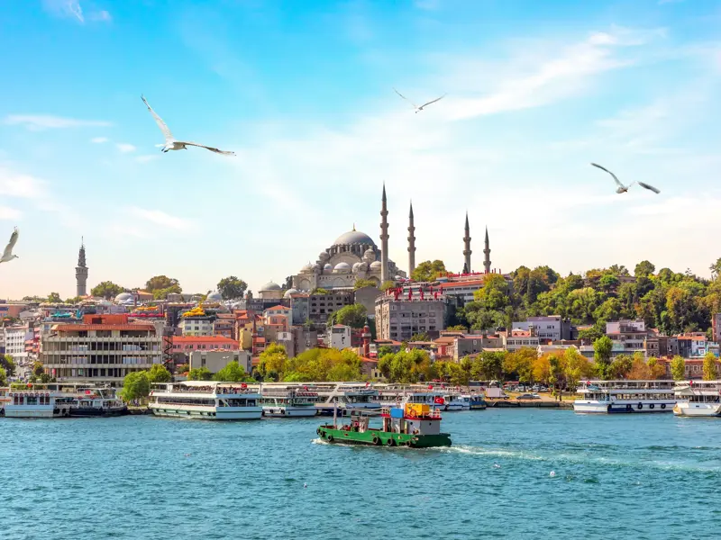 Eine Fähre überquert den Bosporus vor der Skyline Istanbuls mit der dominanten Süleymaniye-Moschee bei sonnigem Wetter.