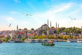 Eine Fähre überquert den Bosporus vor der Skyline Istanbuls mit der dominanten Süleymaniye-Moschee bei sonnigem Wetter.