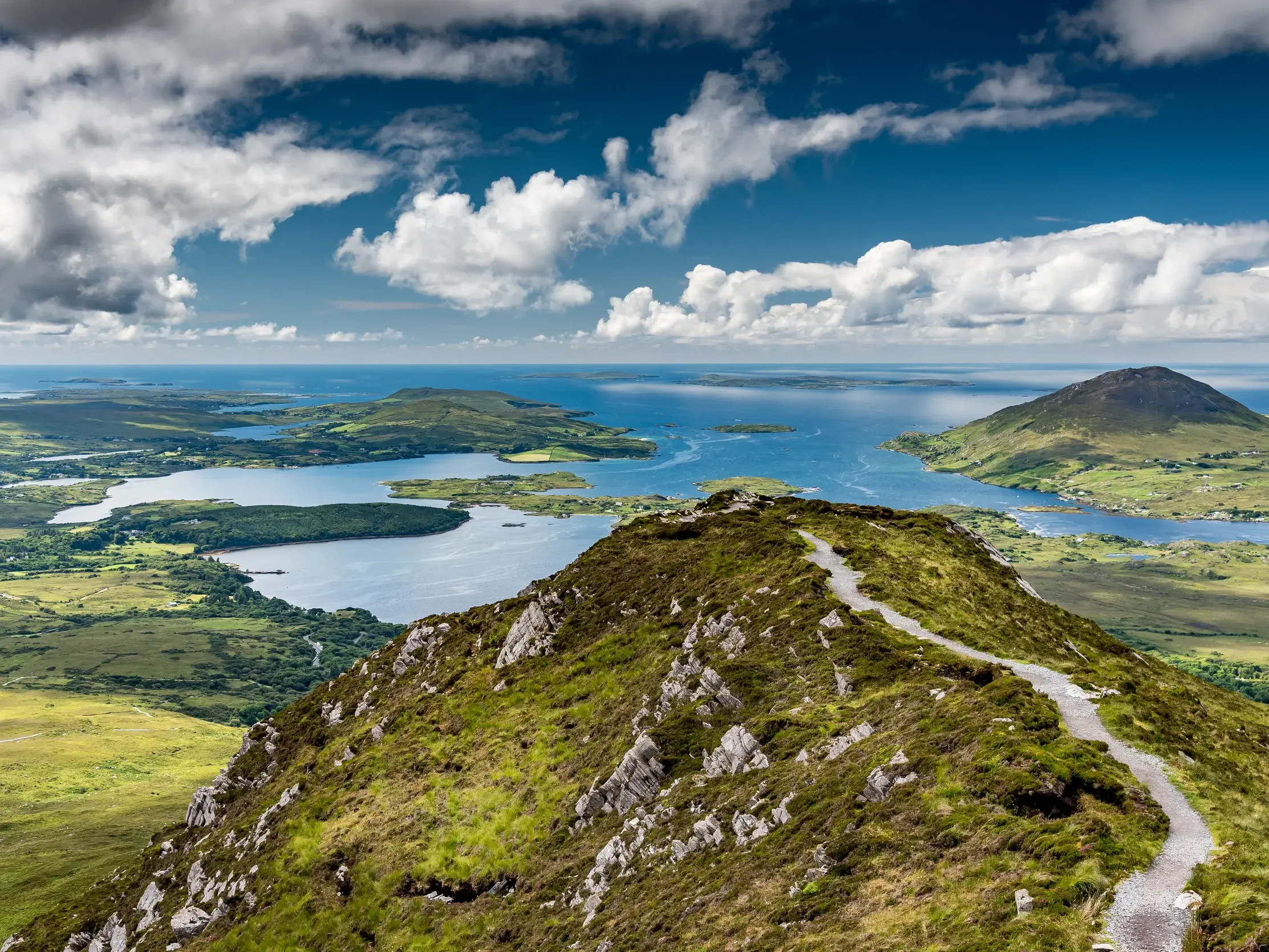 Schmaler Wanderpfad auf dem Grat des Diamond Hill mit weitem Panoramablick über die Küste und Seen des Connemara-Nationalparks.