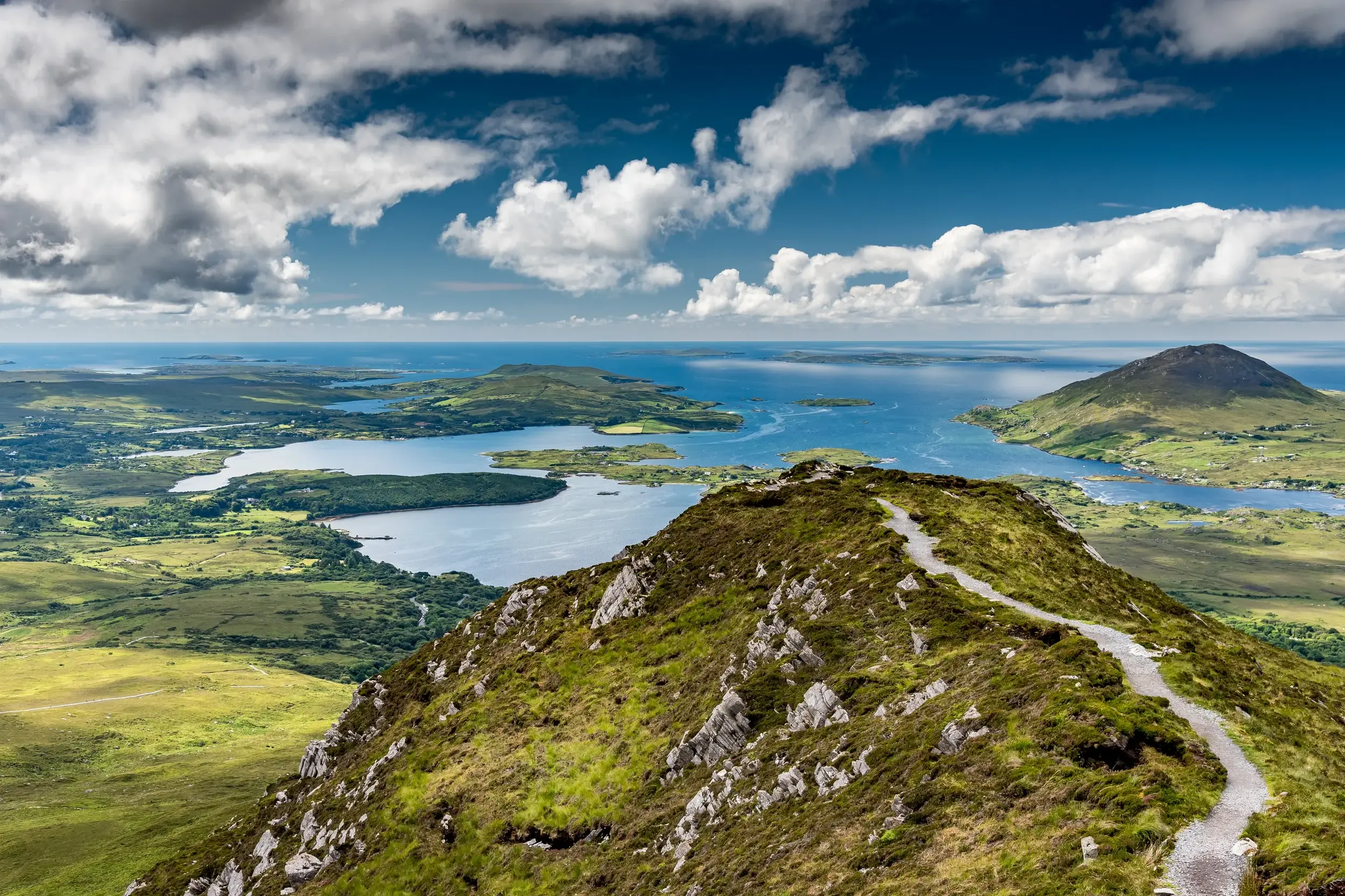 Schmaler Wanderpfad auf dem Grat des Diamond Hill mit weitem Panoramablick über die Küste und Seen des Connemara-Nationalparks.