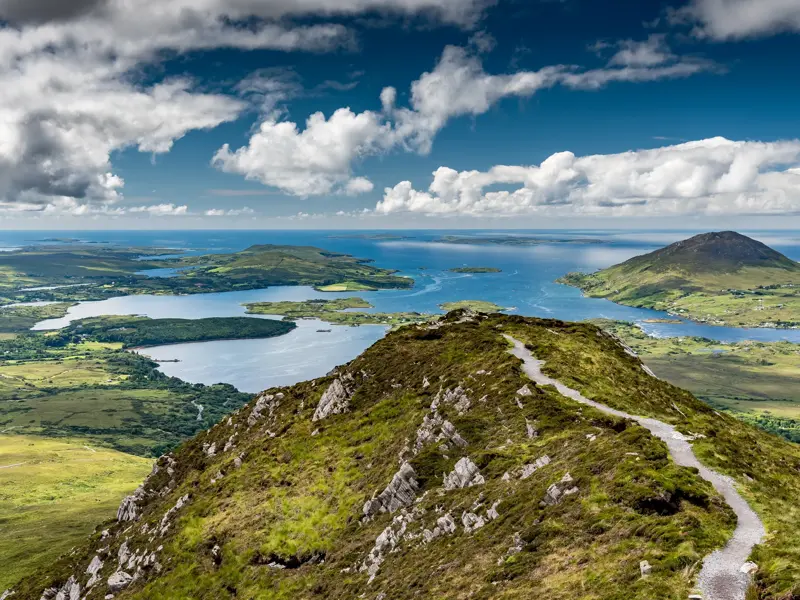 Schmaler Wanderpfad auf dem Grat des Diamond Hill mit weitem Panoramablick über die Küste und Seen des Connemara-Nationalparks.