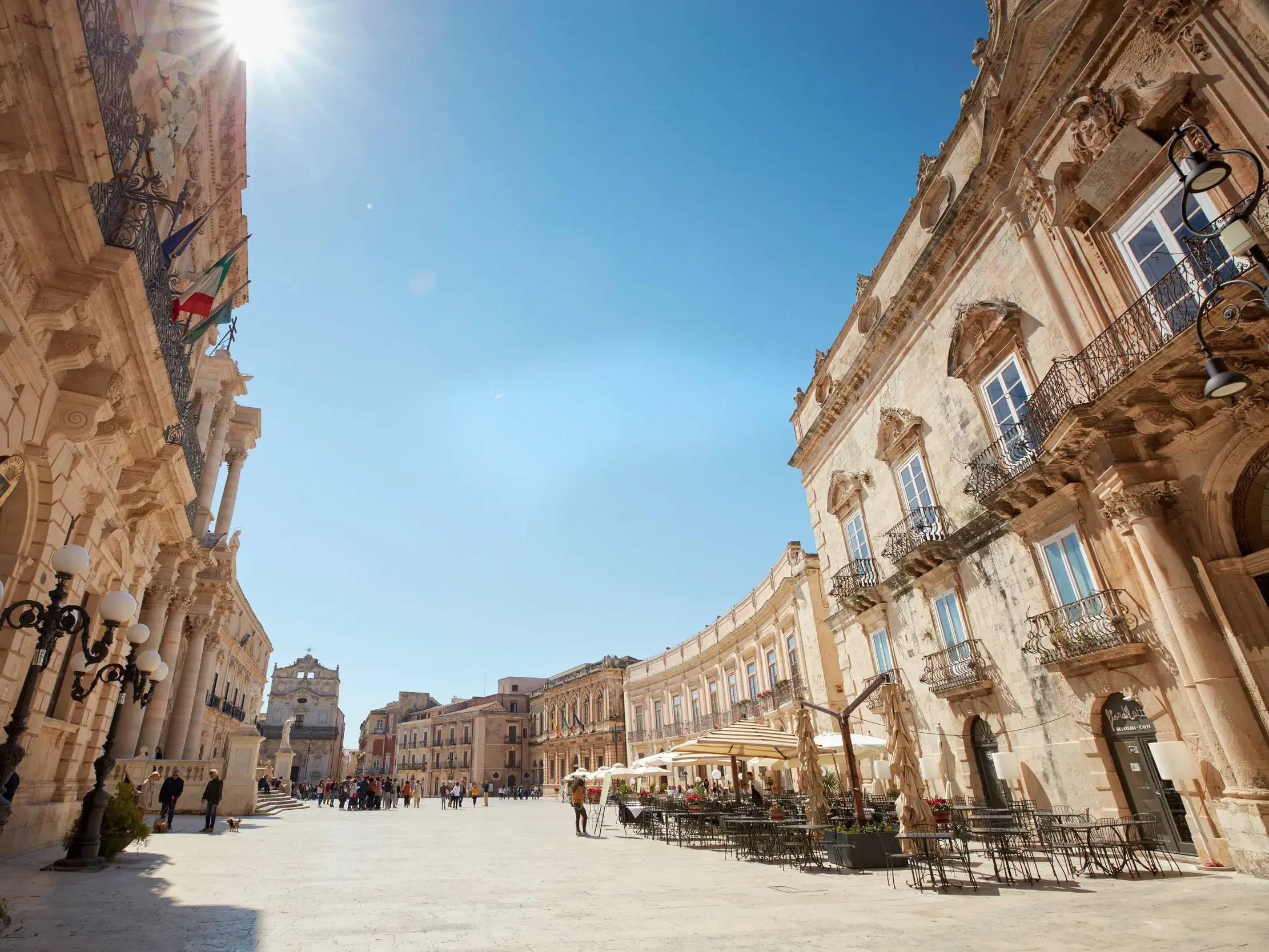 Sonniger Domplatz in Syrakus' Altstadt Ortygia, gesäumt von barocken Palästen und belebten Straßencafés.