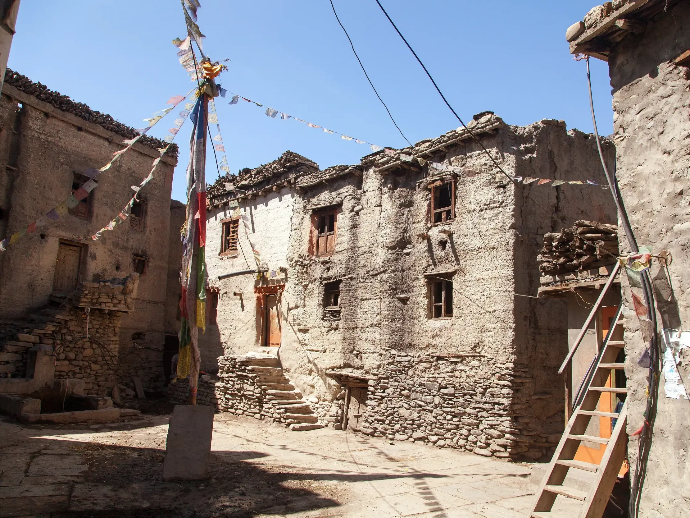 Traditionelle Lehm- und Steinhäuser mit bunten Gebetsfahnen in einer Gasse in Lo Manthang, Königreich Mustang.