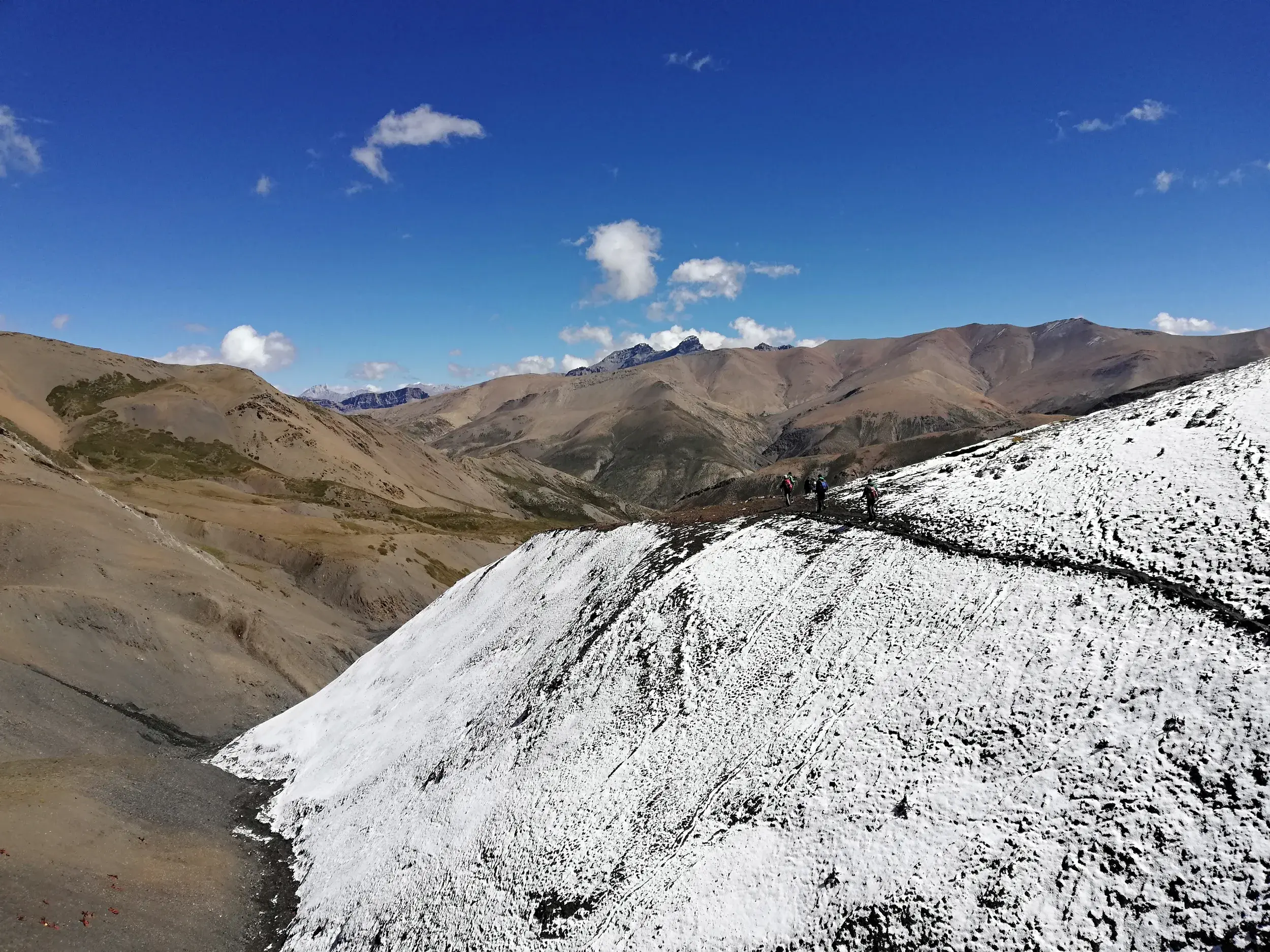 Drei Trekker auf einem schmalen Grat während einer Passüberquerung im kargen, schneebedeckten Dolpo-Gebirge in Nepal.
