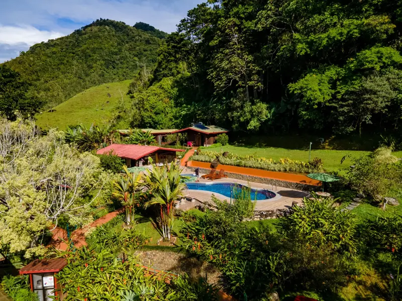 Blick auf das Hotel El Pelicano in San Gerado de Rivas mit Pool und tropischem Garten vor den bewaldeten Bergen Costa Ricas.