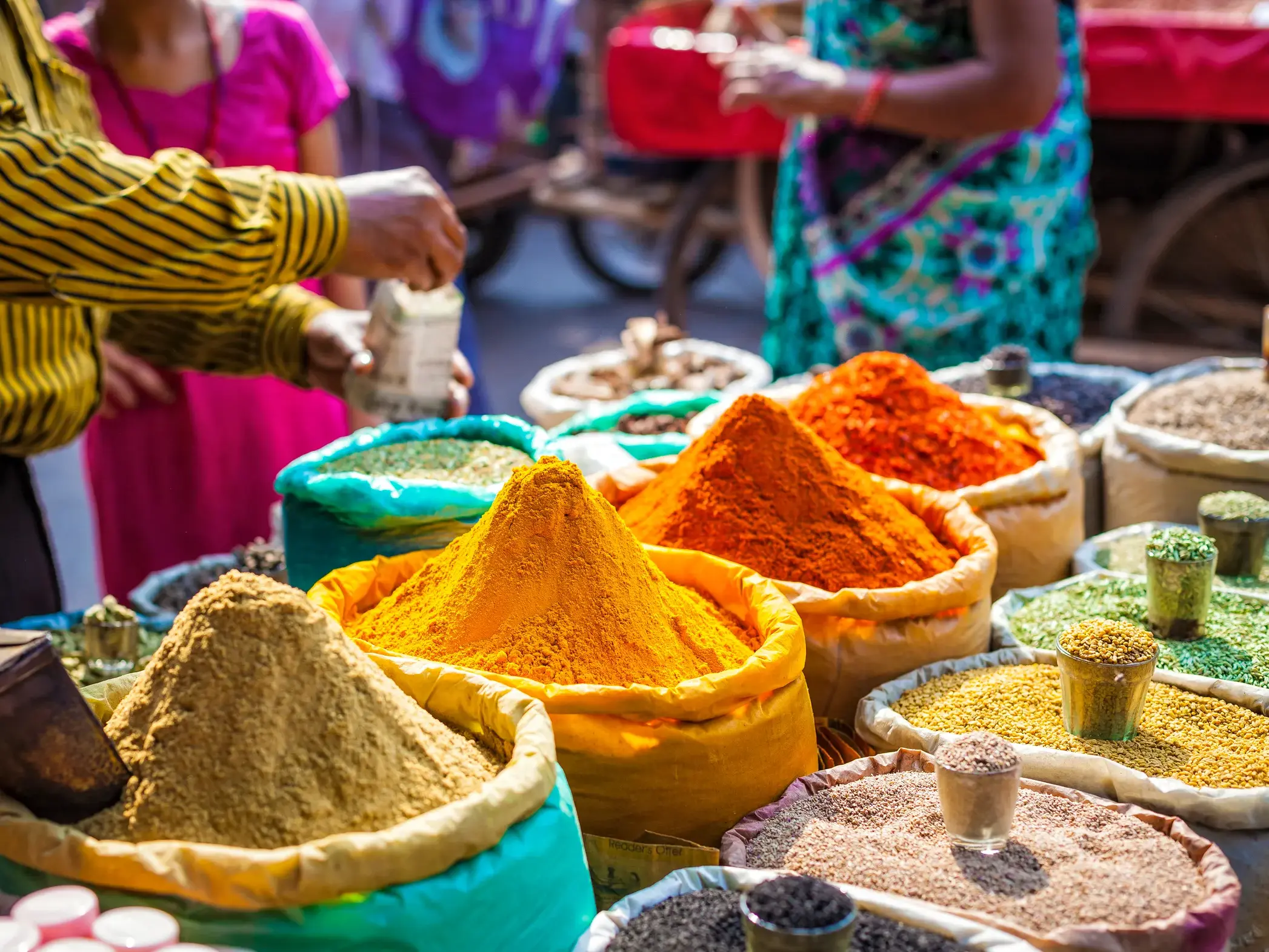 Lebhafter Gewürzmarkt in Jaipur mit bunten Bergen aus Kurkuma und Chili in Säcken, ein Händler bedient eine Kundin.