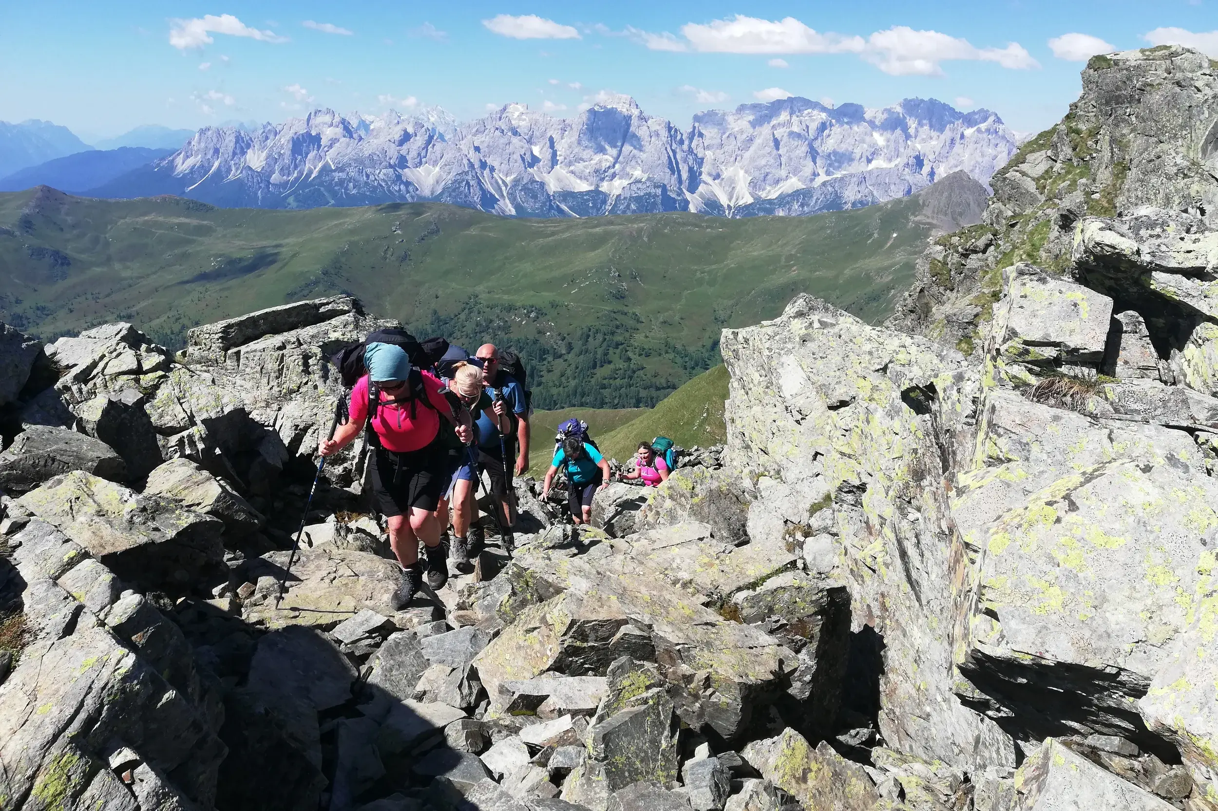 Eine Hauser-Wandergruppe beim Trekking auf einem felsigen Grat des Karnischen Höhenwegs mit Panoramablick auf die Dolomiten.