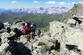 Eine Hauser-Wandergruppe beim Trekking auf einem felsigen Grat des Karnischen Höhenwegs mit Panoramablick auf die Dolomiten.