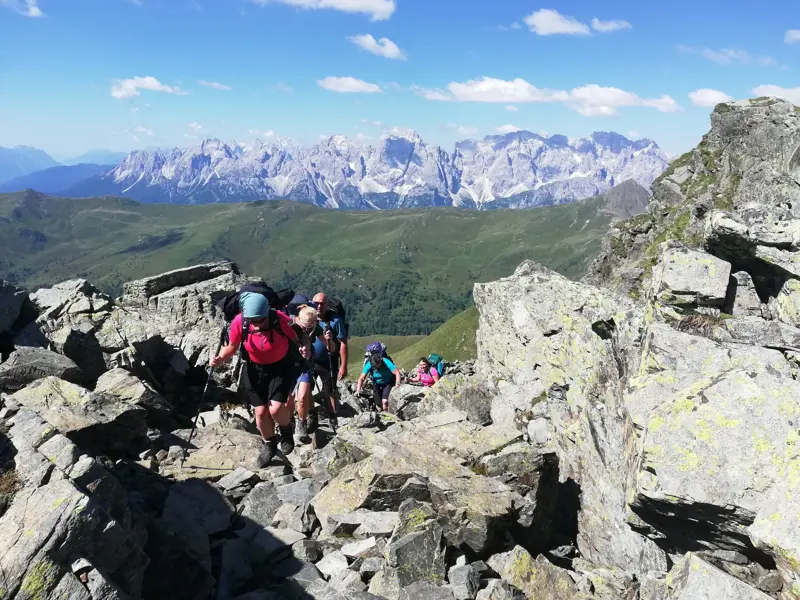 Eine Hauser-Wandergruppe beim Trekking auf einem felsigen Grat des Karnischen Höhenwegs mit Panoramablick auf die Dolomiten.