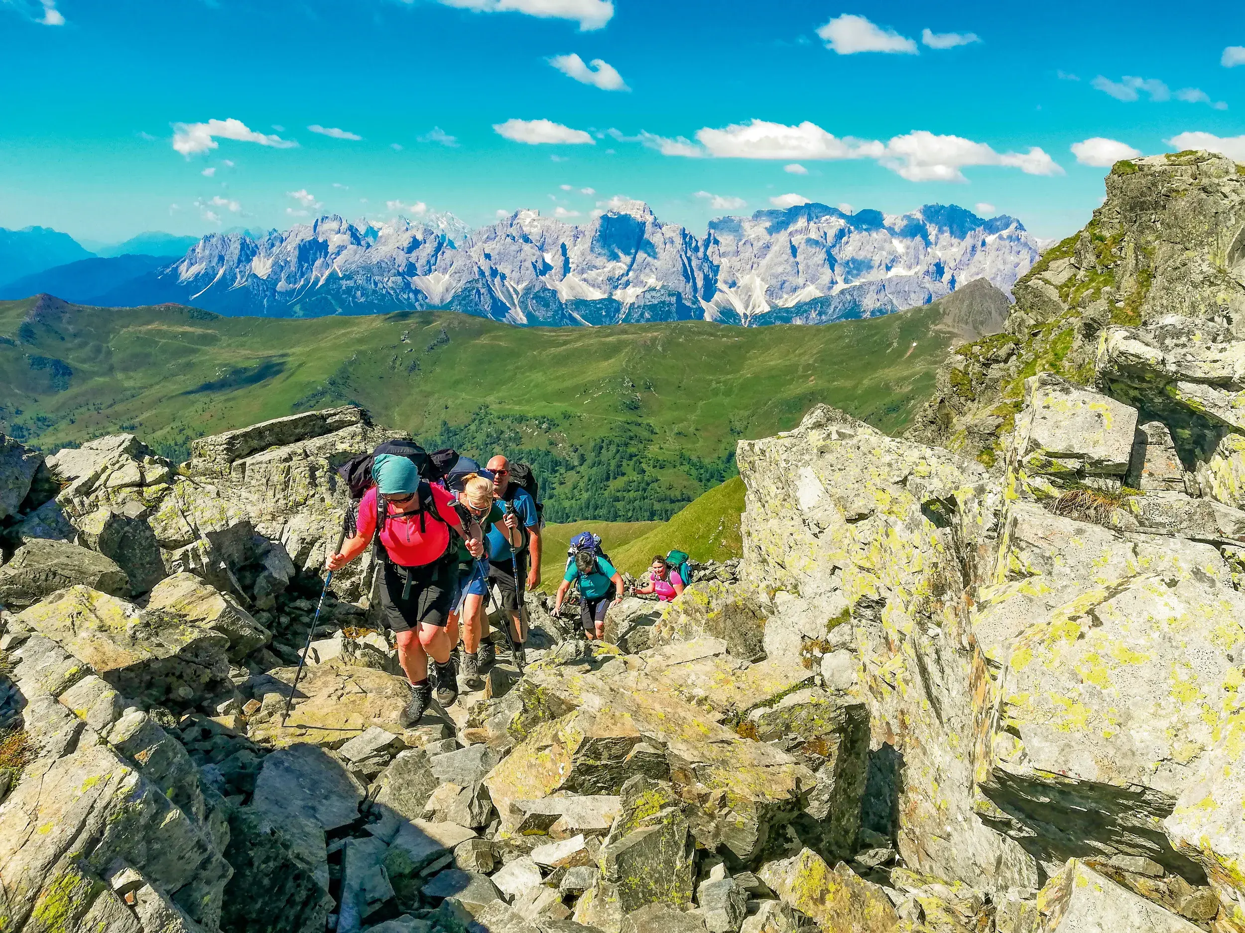 Wandergruppe steigt über einen felsigen Pfad auf dem Karnischen Höhenweg mit Panoramablick auf die Südtiroler Dolomiten.