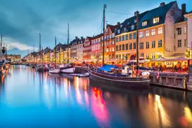 Stimmungsvolle Abenddämmerung am Nyhavn in Kopenhagen mit bunten Giebelhäusern und Cafés, die sich im Kanal spiegeln.